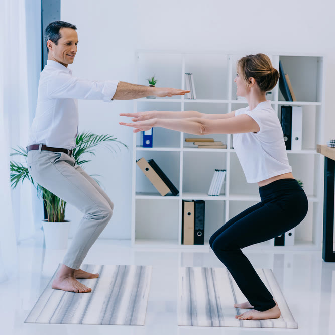 Corporate yoga in Hartford: two colleagues in work clothes holding chair pose on yoga mats in an office