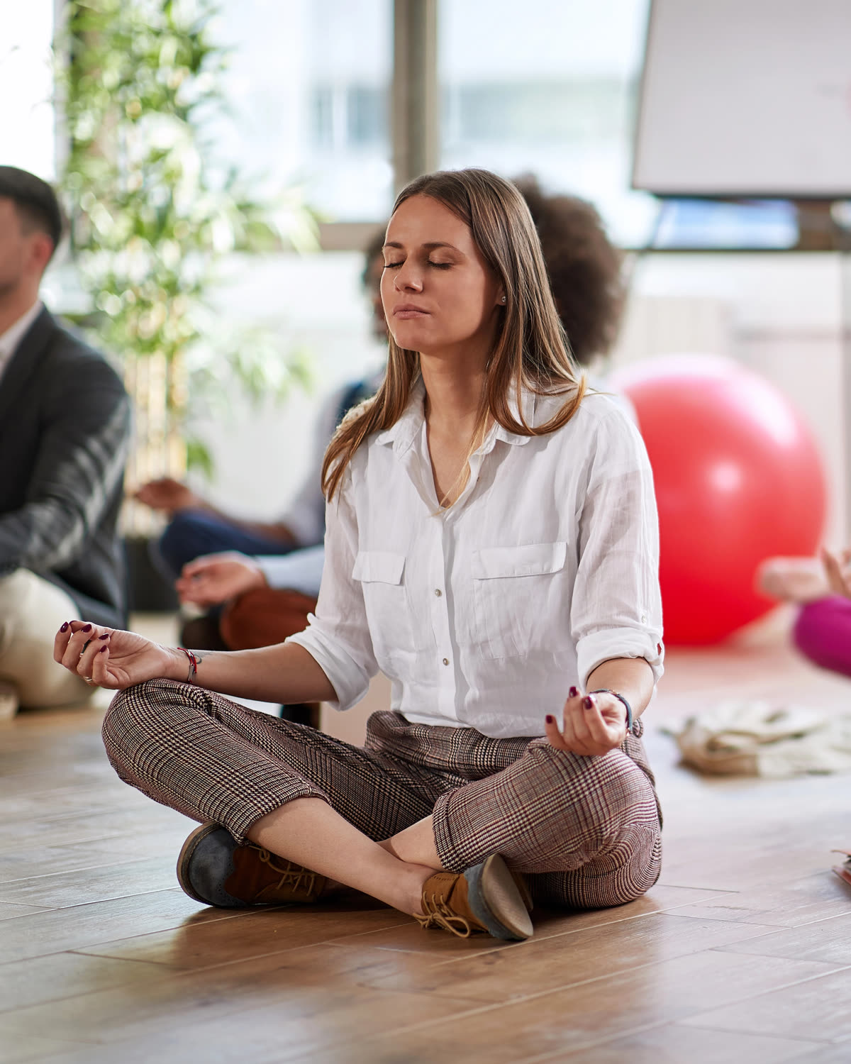 Office meditation in Hartford: a woman in work clothes seated cross-legged with her eyes closed among colleagues